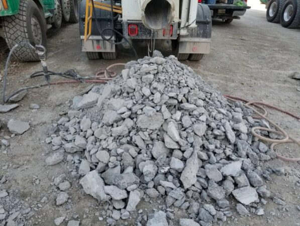 Pile of chipped-out concrete near handheld jackhammers and fleet of redi mix concrete trucks